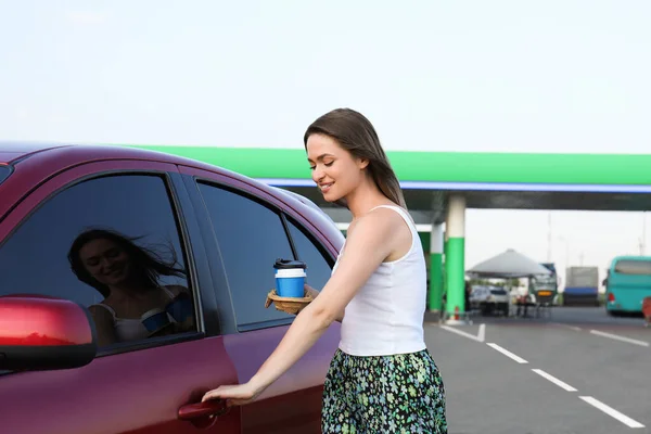 ガソリンスタンドでコーヒーオープンカーのドアを持つ美しい若い女性 — ストック写真