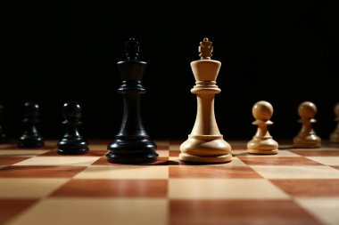Siyah arka plana karşı tahta satranç tahtasında piyonları olan papazlar