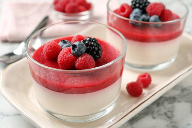 Meyve soslu lezzetli panna cotta ve beyaz mermer masada servis edilen taze böğürtlenler, yakın plan.