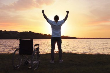 Adam günbatımında tekerlekli sandalyenin yanında el kaldırıyor. İyileştirme mucizesi
