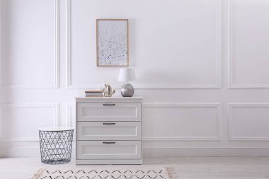 Beyaz duvarın yanında kitap ve lamba bulunan ahşap çekmeceler, yazı için yer. İç tasarım