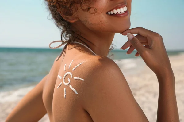 African American woman with sun protection cream on shoulder at beach, closeup