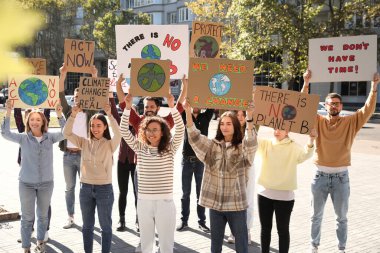 Şehir sokaklarında iklim değişikliğini protesto eden posterleri olan bir grup insan.