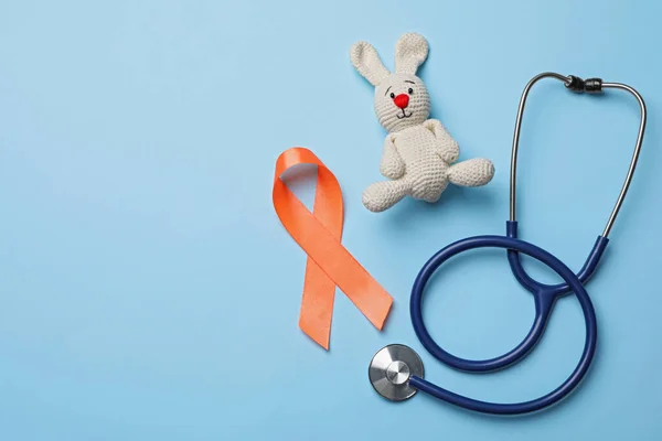 Orange ribbon, toy bunny and stethoscope on light blue background, flat lay with space for text. Multiple sclerosis awareness