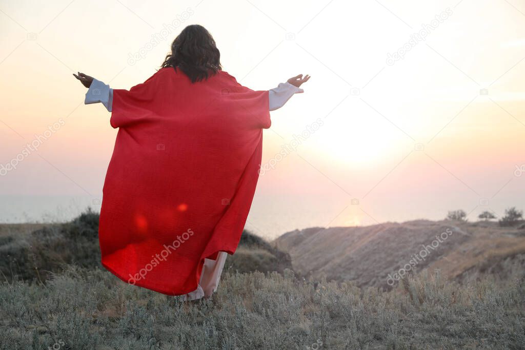 Jesus Christ raising hands on hills at sunset, back view. Space for text