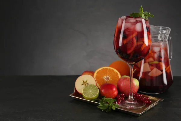 Glass and jug of Red Sangria with fruits on black table, space for text