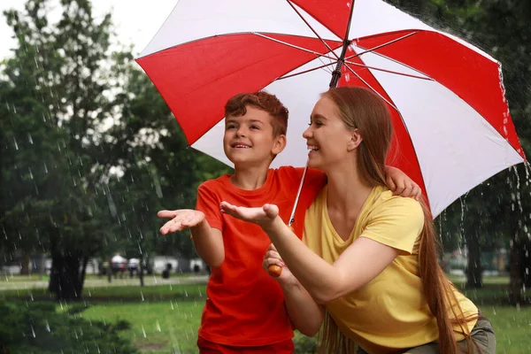 公園で雨の下を歩く傘を持つ母親と息子 — ストック写真