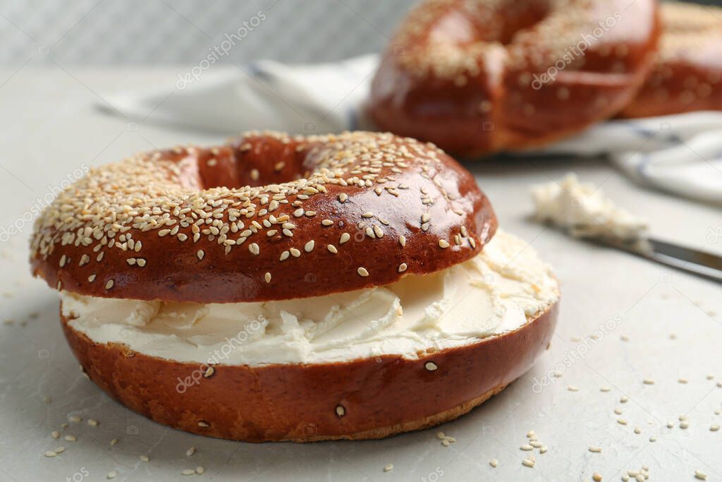 Delicious bagel with cream cheese on light table, closeup