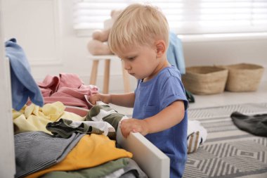 Evdeki elbise çekmecesinde kıyafetlerle oynayan sevimli küçük çocuk.