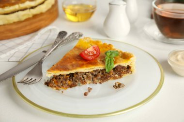 Beyaz masada servis edilen kıymalı, domatesli ve fesleğenli lezzetli turta.