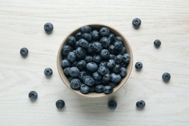 Beyaz ahşap masada yaban mersinli seramik kase, düz. Mutfak aletleri