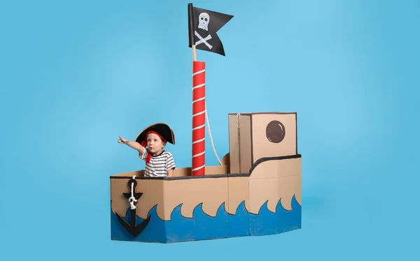 トルコ石の背景に海賊の段ボール船で遊んでかわいい男の子 — ストック写真