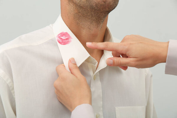 Woman pointing at lipstick kiss mark on her husband's shirt, closeup