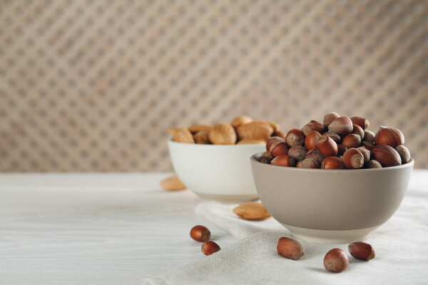 Ceramic bowl with hazelnuts on white wooden table, space for text. Cooking utensil