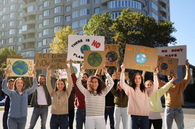 Şehir sokaklarında iklim değişikliğini protesto eden posterleri olan bir grup insan.