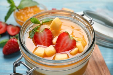 Mango soslu nefis panna cotta ve açık mavi masada taze meyve parçaları, yakın plan.