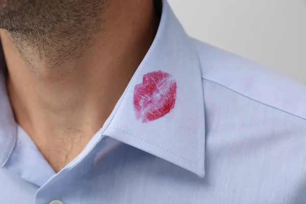 Man in shirt with lipstick kiss mark on white background, closeup