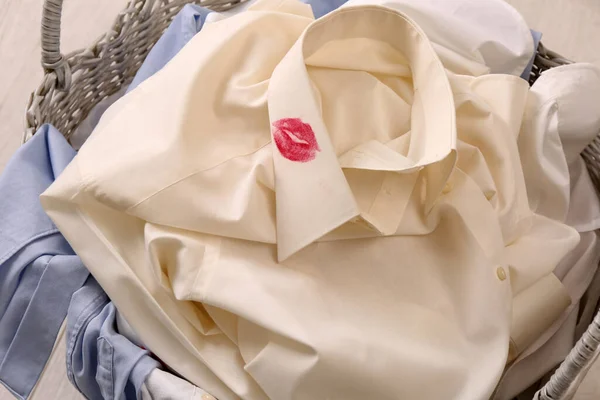 Men's shirt with lipstick kiss marks among other clothes in laundry basket indoors, closeup