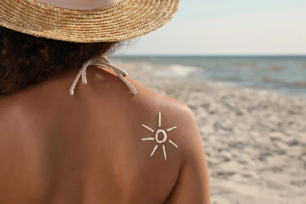 African American woman with sun protection cream on shoulder at beach, back view