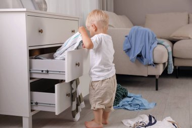 Evdeki elbise çekmecesinde kıyafetlerle oynayan sevimli küçük çocuk.