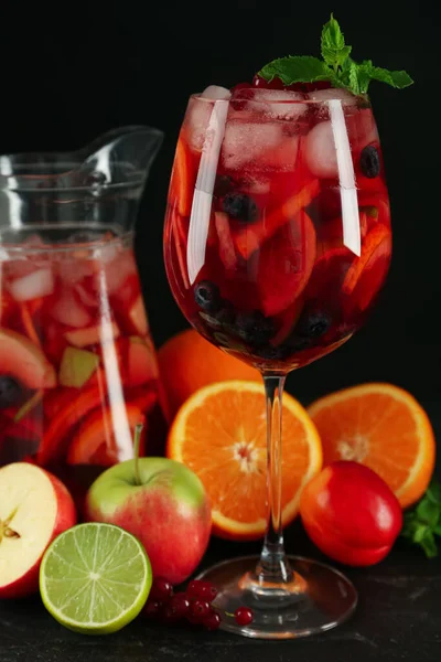 Glass and jug of Red Sangria with fruits on black table
