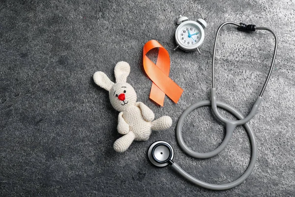 Orange ribbon, toy bunny, stethoscope and alarm clock on grey table, flat lay with space for text. Multiple sclerosis awareness