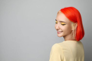 Açık gri arka planda parlak boyalı saçları olan güzel bir genç kadın. Mesaj için yer var.