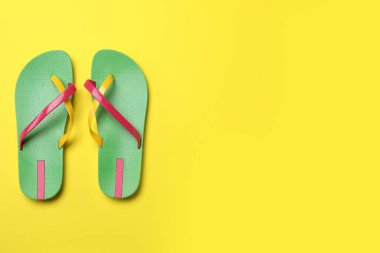 Sarı arka planda şık parmak arası terlikler, düz yatış. Metin için boşluk