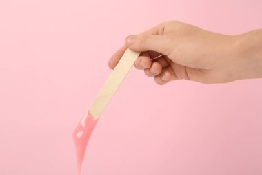 Pembe arka planda sıcak tüy döken bir spatula tutan kadın, yakın plan.