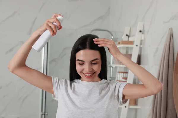 Woman applying dry shampoo onto her hair in bathroom