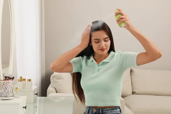 Woman applying dry shampoo onto her hair at home