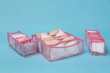 Açık mavi arka planda iç çamaşırları olan şeffaf organizatörler