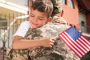 Asker ve küçük oğlu Amerika bayrağıyla dışarıda kucaklaşıyorlar.