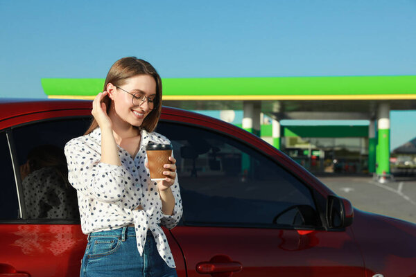 Beautiful young woman with coffee near car at gas station
