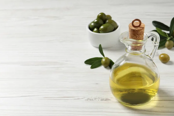 Glazen Kan Olie Rijpe Olijven Groene Bladeren Witte Houten Tafel — Stockfoto