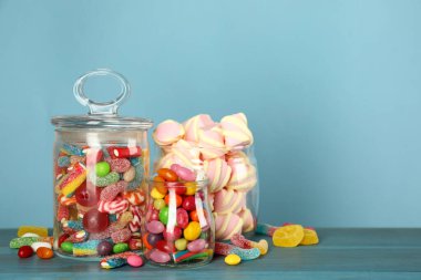 Turkuaz ahşap masada farklı lezzetli şekerlerle dolu kavanozlar, metin için yer.