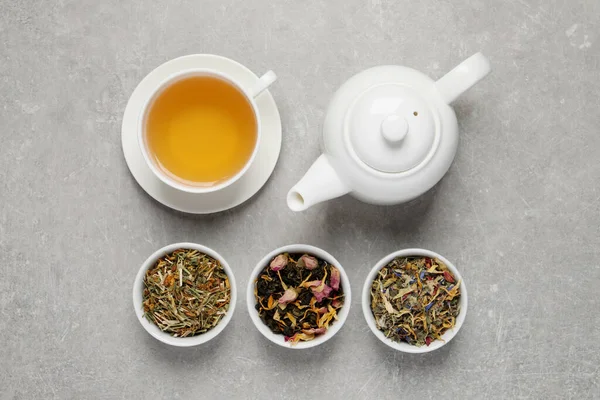 Fresh brewed tea and dry leaves on light grey background, flat lay