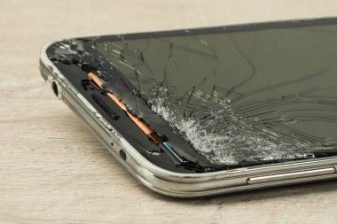 Açık bej ahşap arka planda çatlak ekranlı akıllı telefon, yakın plan. Aygıt onarımı
