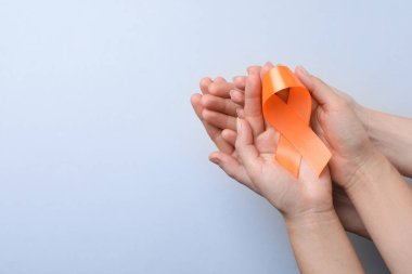 Açık gri arka planda turuncu kurdeleli çift, üst manzaralı mesaj için yer var. Çoklu skleroz farkındalığı