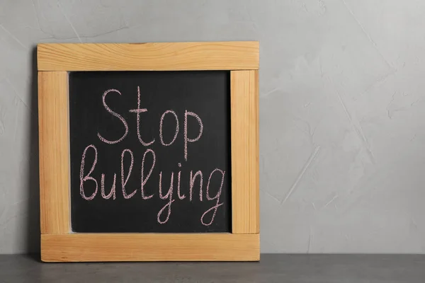 Blackboard Φράση Stop Bullying Στο Τραπέζι Κοντά Γκρι Τοίχο — Φωτογραφία Αρχείου