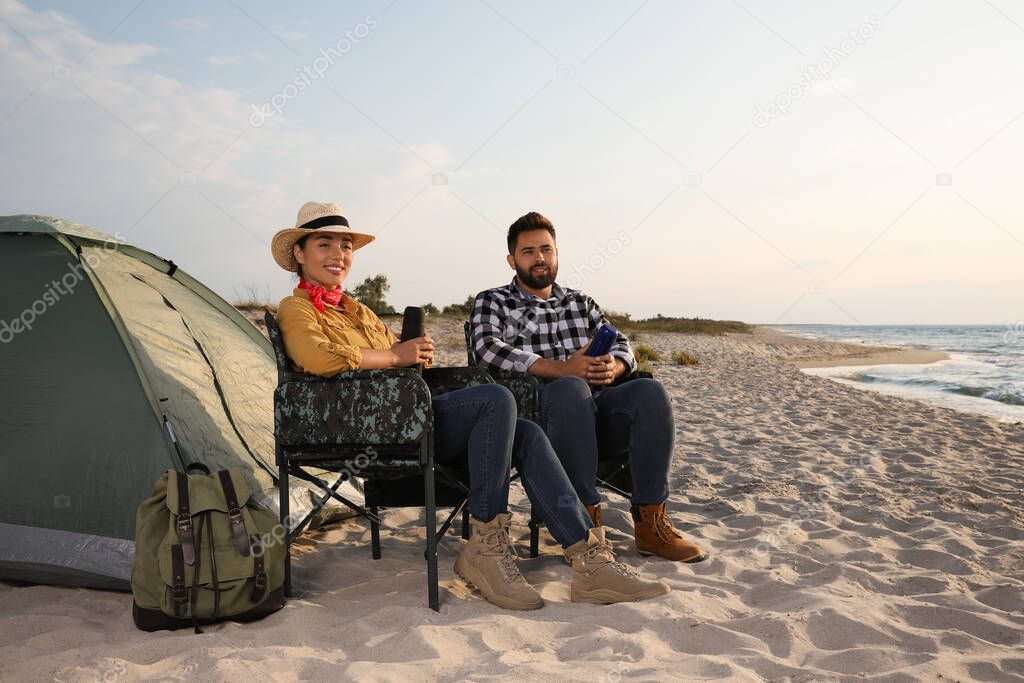 Couple with thermoses near camping tent on beach