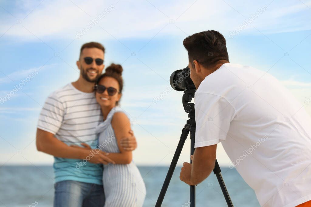 Photographer taking picture of couple with professional camera near sea