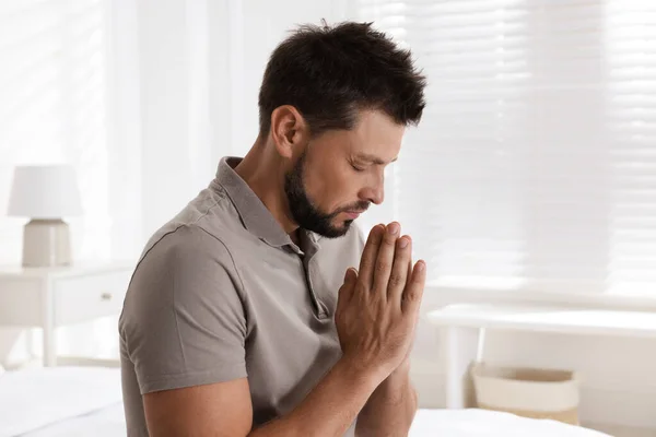 Religious man with clasped hands praying at home