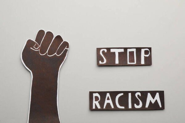 Фраза "Остановить расизм" у бумажной руки со сжатым кулаком на светлом фоне, плоская лежачая