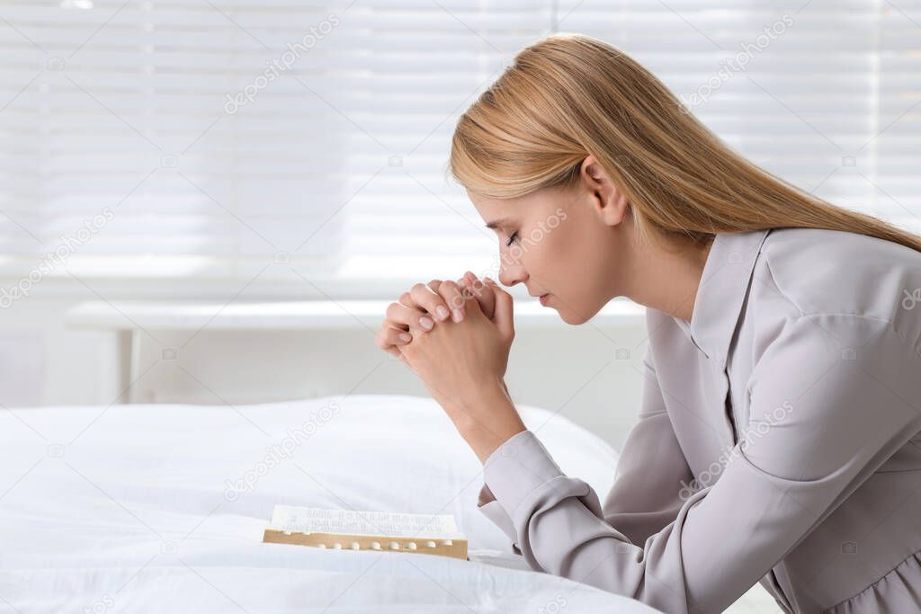 Religious young woman with Bible praying in bedroom. Space for text