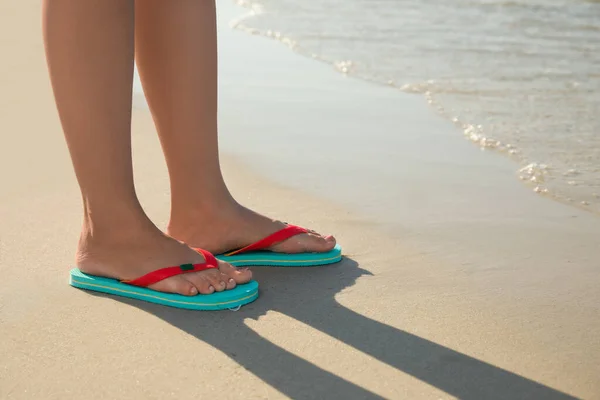 Woman wearing flip flops on sandy beach, closeup