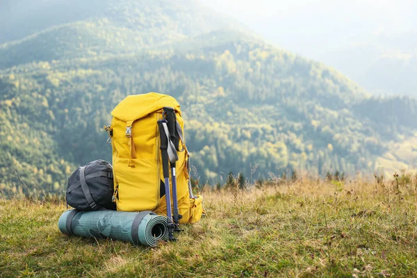 Backpack, trekking poles and sleeping mat in mountains, space for text. Tourism equipment