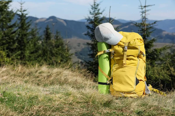 Backpack with sleeping mat and cap on grassy hill, space for text. Mountain tourism