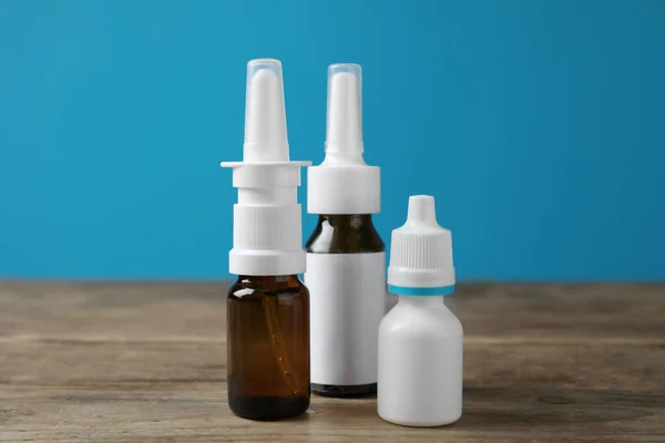 Nasal sprays in different bottles on wooden table against light blue background