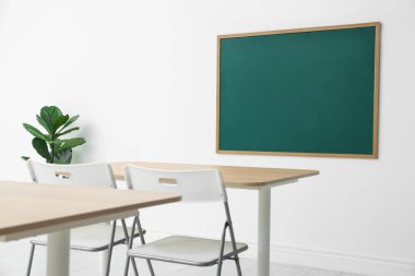 Boş yeşil karatahta, masalar, sandalyeler ve bitkiler sınıfta